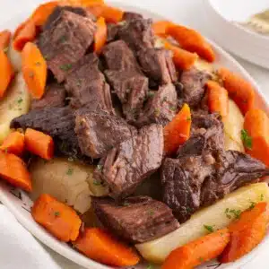 pot roast on platter with carrots and potatoes.