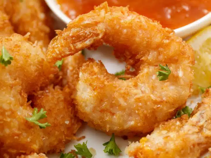 Air-fryer coconut shrimp on plate with dipping sauce.