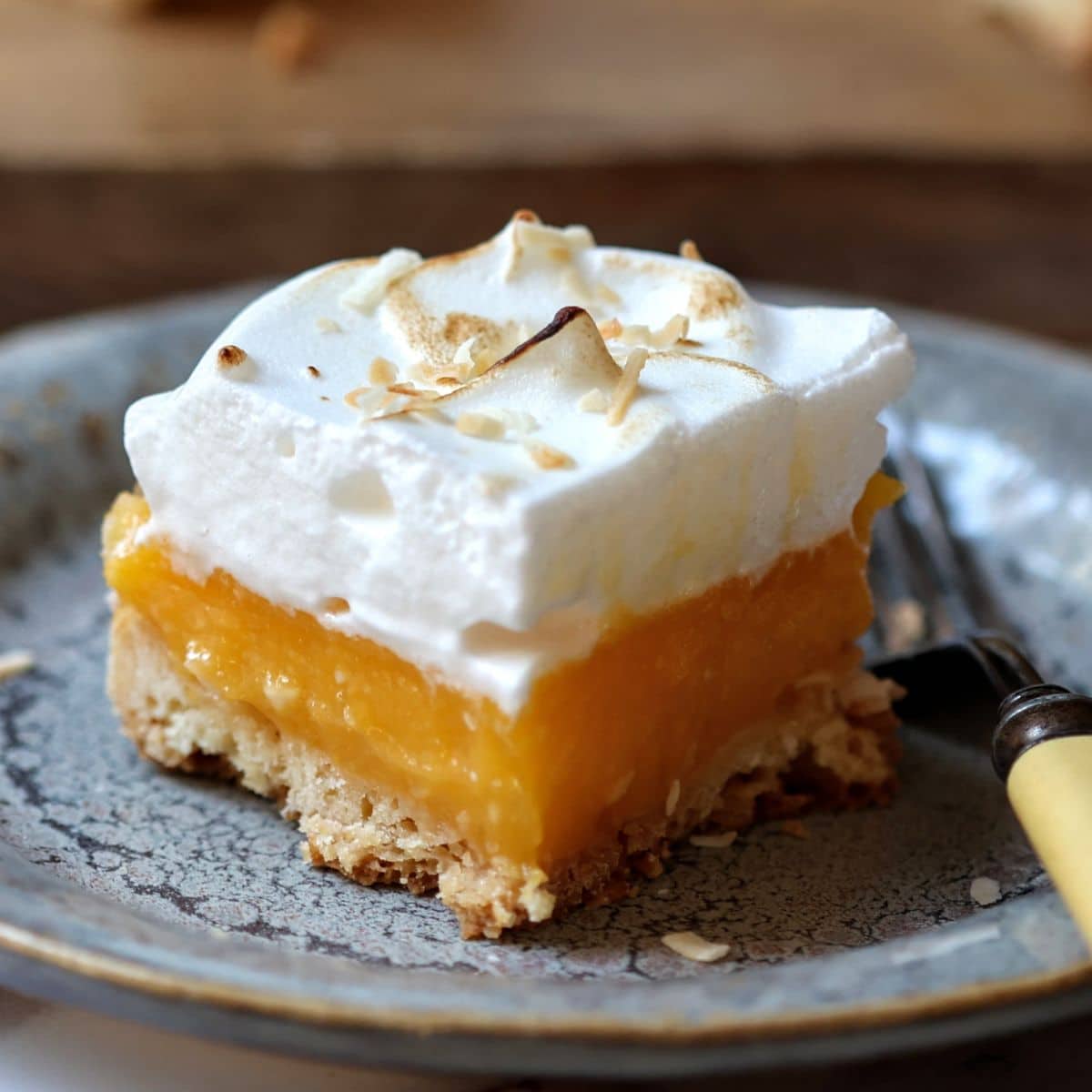 Close up of lemon meringue bar on plate with fork.