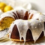 Lemon bundt cake on serving platter with a piece being removed.