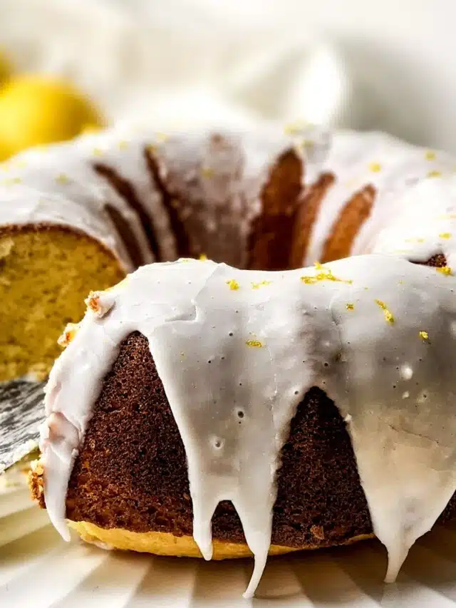 Lemon bundt cake on serving platter with a piece being removed.