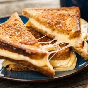 Stack of 2 grilled cheese sandwiches on plate cut in half with cheese dripping