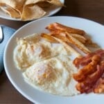 over easy eggs on a plate with bacon and potatoes.