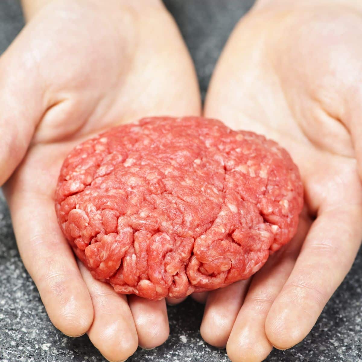 Hands holding uncooked hamburger patty.