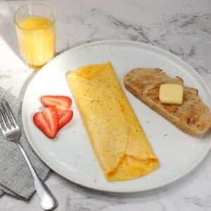 Cheese omelet on a plate with slice of toast and sliced strawberries.