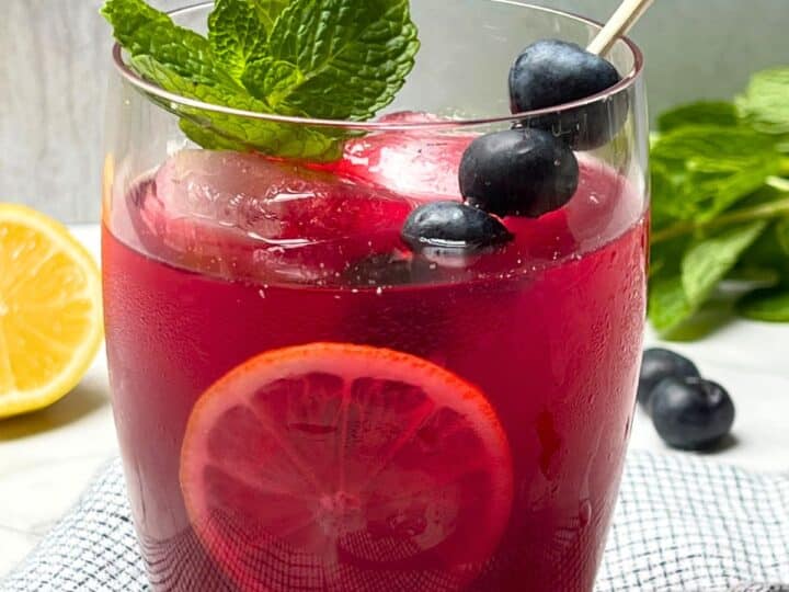 Glass of blueberry-goner lemonade garnished with berries, lemon and mont
